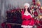 Mrs. Santa holds a cane and a gift on fir tree and piano Christmas background. Holiday