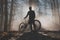 MTB or mountain biker posing in misty forest with sun behind him. Silhouette of a mountain biker in the foggy woods, beautiful