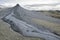 Mud volcano eruption in arid land with grey clouds in background