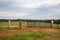 A muddy dirt road leads through an open gate out to a farm pasture on a gently rolling hill