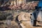 Muddy four-wheel drive vehicle on curving dirt road driving towards colorful cliffs in a high desert landscape