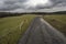 Muddy road between pastures under storm clouds