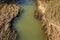 Muddy stream flowing across the field of long dried grass - horizontal