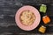 Muesli in a pink plate, kiwi juice, carrot juice, apple puree, wooden dark background. View from above. space for text.