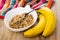 Muesli, spoon in bowl, napkin, bananas on wooden table