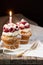 Muffins with soft cream and fresh raspberry powdered with sugar and decorated with burning candle, happy birthday card, rustic