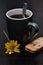 A mug of black coffee with a stack of biscuits and a yellow flower
