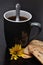 A mug of black coffee with a stack of biscuits and a yellow flower