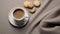 a mug of cappuccino and beige cookies neatly arranged on a saucer, the composition on a tablecloth in either gray, white