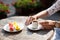 A mug of coffee in hand on table and a delicious eclair on a plate