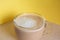 Mug of coffee with milk and froth on a yellow background. Energy and cheerfulness in the morning