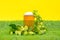 Mug of cold, refreshing foam beer stands on green grass of artificial lawn on yellow background, decorated with clusters