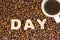Mug with flavored brewed coffee standing on scattered roasted brown coffee beans next to the word day, collected from large 3D let