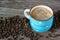 A mug with frothy, aromatic, hot coffee stands on an old wooden textured table. Roasted, fragrant coffee beans lie nearby.