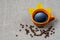 A mug of hot black royal coffee, fallen yellow leaves and coffee beans next to a fabric background. AUTUMN theme