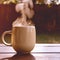 Mug of hot drink steams in sunlight on wooden table during Fall season. AI Image