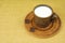 A mug with milk on a saucer and two pieces of chocolate on a table covered with burlap. Pottery on the table