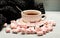 Mug and sweets near cozy knitted scarf. Mug filled with black brewed tea, spoon and heap of marshmallow on white wooden