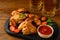 Mugs with beer, delicious baked chicken wings and sauce on wooden table