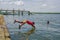 Muisne, Ecuador - March 16, 2016: Kids diving and swimming in pacific ocean from stone surface with clothes on