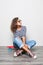 Mulatto mixed race young girl with curly hair seats on floor and holds skateboard posing on white background