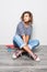 Mulatto mixed race young girl with curly hair seats on floor and holds skateboard posing on white background