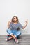 Mulatto mixed race young girl with curly hair seats on floor and holds skateboard posing on white background