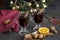 Mulled wine in glasses at black background. Fir wreath, lights, tray with orange, cinnamon, nuts, cone, spices