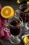 Mulled wine in glasses at black background. Fir wreath, tray with orange, cinnamon, nuts, cone and spices near