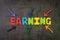 Multi color arrows pointing to the word Earning at the center of black cement chalkboard wall, Business profit or revenue from