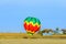 A multi-colored balloon near a farm takes off in a blue sky over