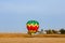 Multi-colored balloon near a farm takes off in a blue sky over a