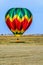 multi-colored balloon soars into the blue sky over the yellow field