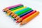 Multi colored bunch of assorted rainbow color pencil line up in a row close together side by side arranged in white background,