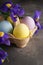 Multi colored Easter eggs in a cardboard box and fresh flower on a wooden background, vertically. Close-up