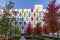 A multi-colored high-rise apartment building with a landscaped yard. Autumn colors of bushes and trees