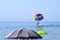 Multi-colored parachute with man on the background of the sea, blue sky and open beach umbrellas. The beginning of the flight by