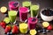 multi-colored smoothies in different glasses stand on a dark wooden table, berries, fruits and greens are cut nearby