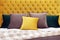 Multi-colored square pillows lie on the bed with a soft yellow velvet headboard with capitones. Selective focus.