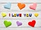 Multi-colored wooden letters making up the inscription I love you and multi-colored origami paper hearts on a white background.