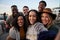 Multi-cultural group of friends taking a selfie at a rooftop party. Close up, smiles with diverse young adults.