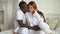 Multi-ethnic couple dressed in white is sitting on the bed in home. Multi-racial couple kisses