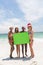Multi-ethnic female friends holding a empty green placard at beach on a sunny day