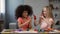 Multi-ethnic girls at kid club, sitting at table and smudging hands with paints