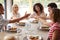 Multi ethnic group of five happy young adult friends laughing and raising glasses to toast during a dinner party