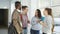 Multi-ethnic group of four students standing in wide lighty glassy hall in college talking to each other in positive way