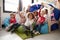 A multi-ethnic group of infant school children sitting on bean bags in a comfortable corner of the classroom, raising their hands