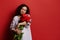 Multi ethnic happy delightful woman in embroidered shirt, posing with a bouquet of tulips,  on red background