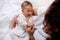 Multi ethnic happy mother cuddling her baby boy, sitting together on the bed in bedchamber interior