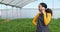 Multi-ethnic woman farmer uses cellphone, talking in greenhouse, organic herbs